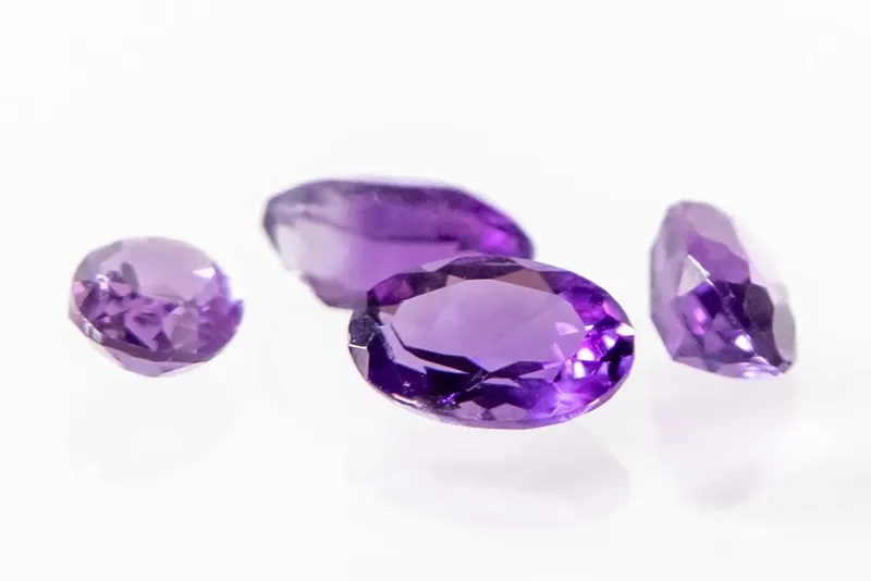 Four oval faceted purple amethysts on a white background
