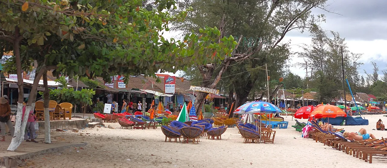 Sun loungers and colourful umbrellas under trees along Ochheuteal Beach in Sihanoukville